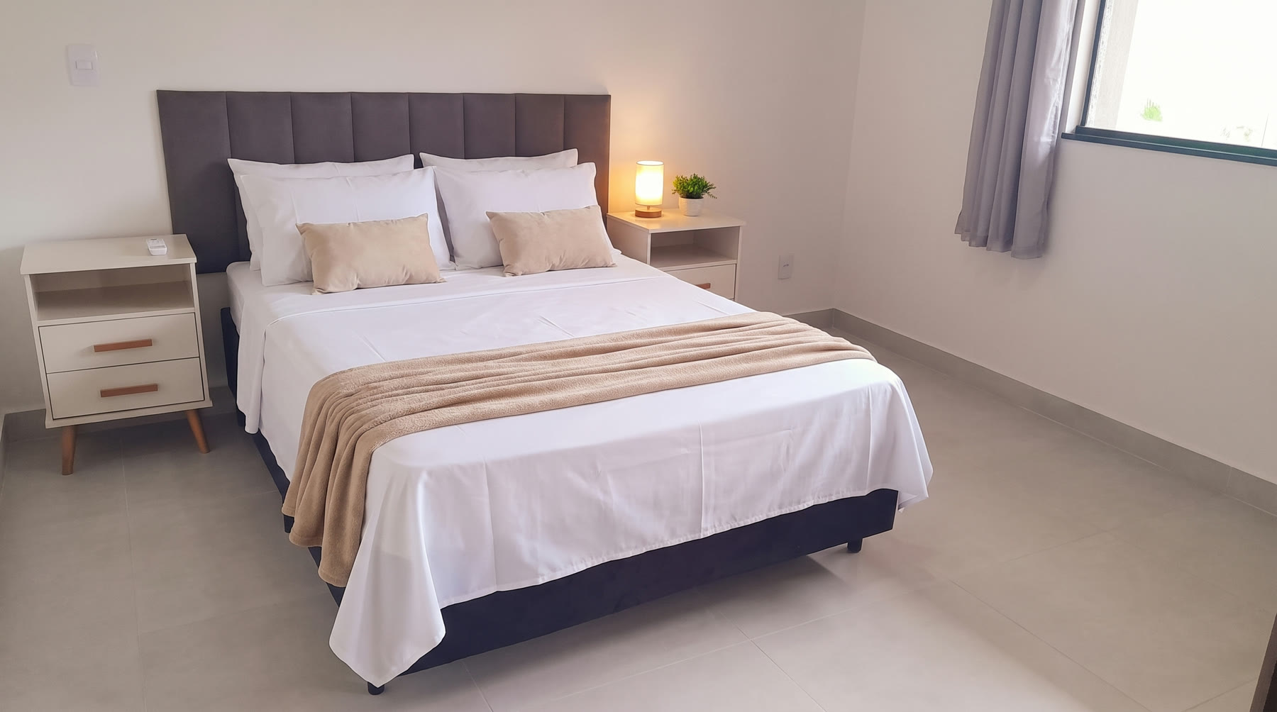 Suíte com cama de casal arrumada, criados-mudos e ar-condicionado